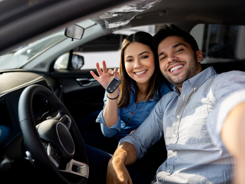 A man and woman sitting in a car's front seats, both appearing attentive and ready for their journey.